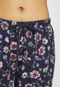 Navy blauwe pyjamabroek met een bloemenpatroon in rood, wit en geel, voorzien van een elastische tailleband en een trekkoord. Zachte stoftextuur.