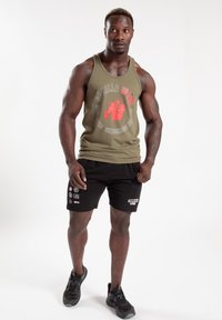 Groen tanktop met grafische print, zwarte shorts met logo's, atletische pasvorm, gedragen met zwarte sneakers, tegen een eenvoudige witte achtergrond.