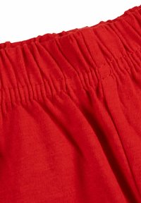 Tessuto rosso con una finitura morbida e testurizzata. La cintura presenta una rielaborazione elastica per elasticità e comfort, visibile sul bordo superiore.