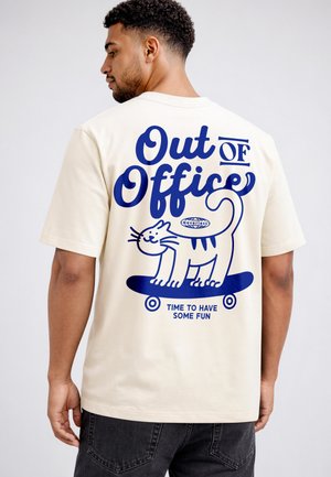 Man wearing cream t-shirt with blue graphic of a smiling cat on a skateboard and text "Out of Office, Time to Have Some Fun."