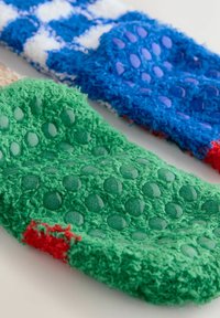 Zwei fusselige Socken: eine grüne mit erhabenen Punkten und roten Akzenten; die andere blaue mit einem weißen Schachbrettmuster und einem strukturierten Abschnitt.