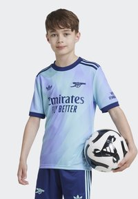 Maillot de football bleu clair avec des accents bleu marine, portant le texte "Emirates Fly Better" et le logo du club. Un ballon de football noir et blanc est tenu sous le bras.