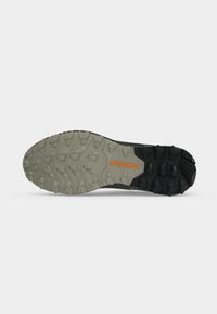 Semelle d'une chaussure de trail avec une semelle crantée beige et noire, comportant le mot "PRESA" en orange près de la semelle intermédiaire.