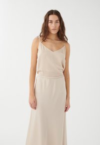 Vestido de satén beige con escote en V y tirantes finos, que cuenta con una cinturilla elástica y una falda larga y fluida. Textura suave.