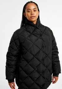 Schwarze gesteppte Daunenjacke mit hohem Kragen, diagonaler Steppnaht und elastischen Bündchen. Das Material wirkt glatt und isoliert.