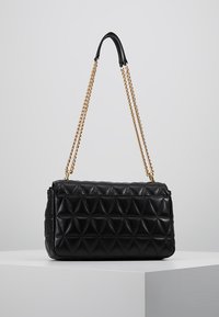 Černá prošívaná kabelka z hladké kůže, s geometrickým trojúhelníkovým vzorem a zlatým řetízkovým popruhem.