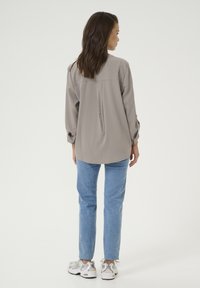 Light gray long-sleeve shirt with a back pleat, paired with light blue jeans and gray sneakers. The fabric appears smooth and lightweight.