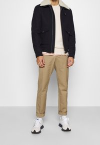 Marinblå ulljacka med en beige fårskinnskrage, två framfickor, bärs över en ljus gräddfärgad tröja och khakifärgade byxor, matchat med vita sneakers.