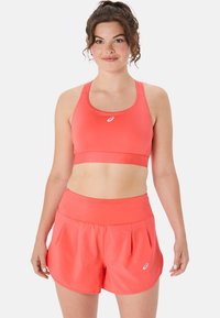 Coral sports bra and matching shorts made of light, stretchy material. The design features a supportive band and pleated shorts for flexibility.