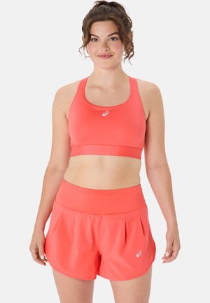 Coral sports bra and matching shorts made of light, stretchy material. The design features a supportive band and pleated shorts for flexibility.