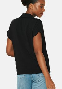 Blusa nera a maniche corte con colletto, caratterizzata da una vestibilità morbida e una texture delicata, abbinata a jeans in denim blu chiaro.