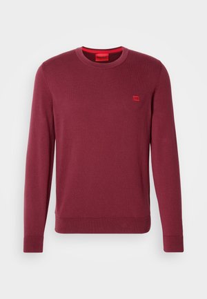 Maglione a maniche lunghe color bordeaux con girocollo, con piccolo patch logo rosso sul petto e etichetta interna rossa, tessuto a maglia semplice.