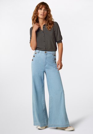 Czarna bluzka w białe groszki z krótkimi rękawami, zestawiona z jasnoniebieskimi, szerokimi spodniami o wysokim stanie, ozdobionymi złotymi guzikami.