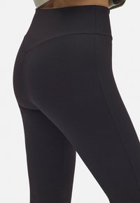 Leggings negros de cintura alta, fabricados con una tela elástica, que cuentan con costuras suaves y una silueta ceñida y elegante. Sin logotipos ni patrones visibles.