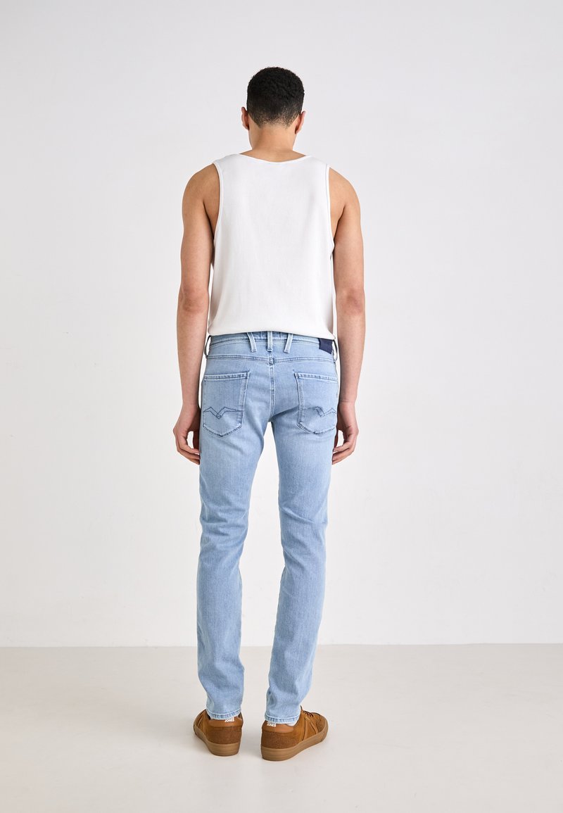 Lichtblauwe jeans met een slim fit, gecombineerd met een witte mouwloze shirt. De jeans hebben achterzakken met stiksels en een donker label.