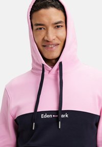 Sweat à capuche en rose et marine. Il comporte une poche kangourou, un design en bloc de couleurs contrastantes et un logo "Eden Park" brodé.