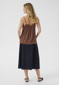 Camisole en soie marron avec des bretelles spaghetti, associé à une longue jupe en denim bleu marine avec des coutures visibles et une silhouette décontractée.