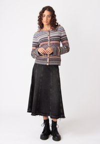 Cardigan lavorato a maglia multicolore con motivi geometrici, bottoni davanti, abbinato a una gonna di jeans nera e stivaletti neri con lacci.