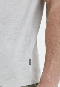 Lys grå T-skjorte med myk, strukturert stoff. Har en side søm etikett med et svart-hvitt stripe mønster. Kortermet design.