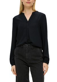 Blusa nera a maniche lunghe con scollatura a V e dettagli plissettati, realizzata in tessuto morbido, abbinata a pantaloni in denim grigio scuro a vita alta.