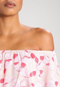Blusa de hombros al descubierto en tejido ligero de color pálido con patrones de hojas en rosa y rojo; corte relajado con escote elástico.