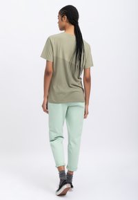 T-shirt verde oliva a maniche corte con una vestibilità leggermente ampia abbinato a pantaloni verdi menta con risvolto. Sneakers nere con suola bianca.