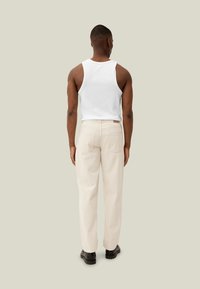 Canottiera bianca da uomo abbinata a pantaloni color crema, con una vestibilità rilassata e dettagli di cucitura visibili. La persona indossa scarpe nere.