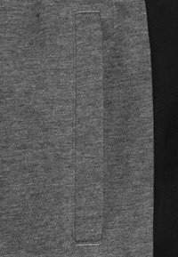 Grijs sweatshirt stof met een opvallend zakdetail, voorzien van een contrasterend zwart zijpaneel. Zachte textuur met subtiele vlekken.