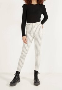 Svart ribbad långärmad topp i kombination med vita randiga högmidjade byxor med bälte, bärs med svarta kraftiga snörkängor.