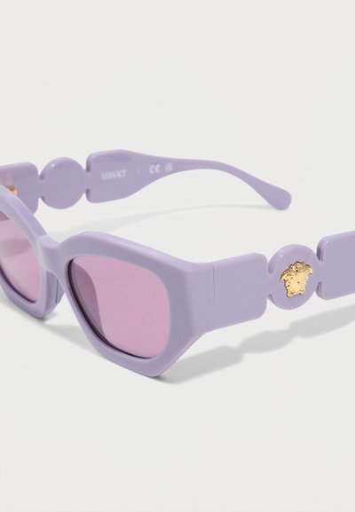 Γυαλιά ηλίου σε σχήμα γάτας σε λιλά απόχρωση με φακούς με μοβ απόχρωση και χρυσό έμβλημα Μέδουσας στα μπράτσα, σε λευκό φόντο.