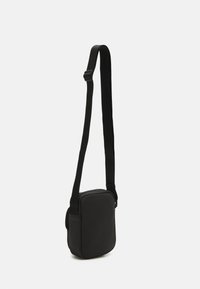 Bolso cruzado negro con forma rectangular, hecho de tela suave. Cuenta con una correa ajustable y un cierre de cremallera. Diseño minimalista.
