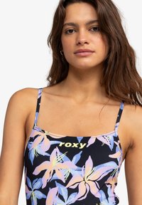 Zwarte bloemen tanktop met een kleurrijk leliepatroon in pink en blauw, met dunne bandjes en "roxy" in het geel gedrukt. Soepele stoftextuur.