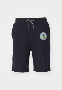 Shorts bleu marine en tissu texturé, avec une taille élastique, un cordon de serrage et un patch circulaire présentant un design graphique coloré.