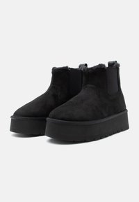 Pair of black suede ankle boots with platform soles and fur lining, featuring elastic side panels and pull tabs on a white background.