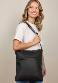 Czarna skórzana torba tote o gładkiej fakturze. Posiada zewnętrzną kieszeń na zamek i długi regulowany pasek. Minimalistyczny design.