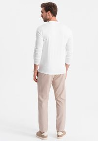 Weißes Langarmshirt, slim fit, kombiniert mit beigen Hosen und hellen Sneakers. Minimalistisches Design, glatte Textur und neutrale Farbpalette.