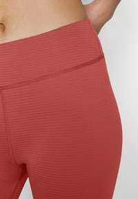 Leggings rossi a vita alta realizzati in un tessuto testurizzato e a coste, con una vita senza cuciture e dettagli di cucitura discreti lungo i bordi.
