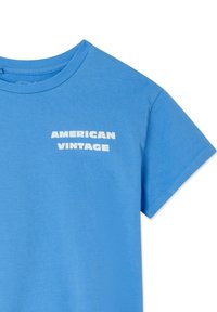 T-shirt en coton bleu clair avec manches courtes et col rond, portant le texte « AMERICAN VINTAGE » en lettres blanches majuscules sur la poitrine.