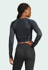 Top corto atletico nero con maniche lunghe, caratterizzato da strisce diagonali e un design aderente, abbinato a leggings neri a vita alta.