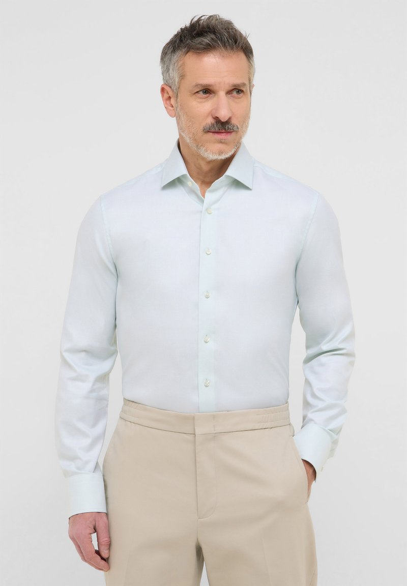 Camicia button-up azzurro chiaro con maniche lunghe e una texture morbida. Presenta un colletto classico e bottoni chiari, abbinata a pantaloni beige.