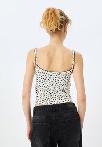Hvid blomstret camisole med sort stikning, med tynde stropper og en tætsiddende pasform, parret med sorte højtaljede jeans.