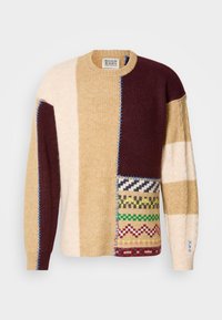 Õmmeldud kampsun, millel on patchwork-disain beežis, burgundias ja kreemjas toonides, erinevate tekstuuride ja geomeetriliste mustritega. Kontrastne sinine õmblemine.