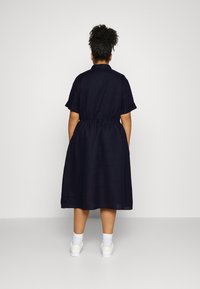 Robe en lin marine avec des manches courtes, une taille cintrée et une jupe évasée, associée à des chaussures de sport blanches et des chaussettes.