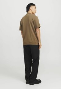 Polo shirt en tricot marron avec des manches courtes, assorti à un pantalon noir et des chaussures noires, vu de dos sur un fond clair.