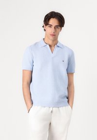 Polo de culoare albastră deschis, cu mânecă scurtă și guler în V, având un design tricotat cu textură și un detaliu mic cu logo pe piept.