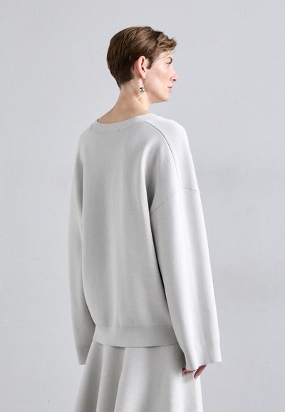 Ανοιχτό γκρι oversized πουλόβερ με φαρδύ στρογγυλό λαιμόκομμα, χαμηλωμένους ώμους και ριβέ κουμπιά, σε συνδυασμό με μια ταιριαστή φούστα. Λείο υλικό.