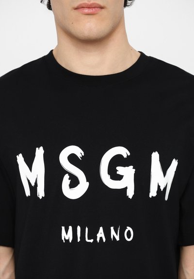 Musta puuvillapaita, jossa on rohkeaa valkoista siveltimien jälkeä "MSGM" tekstin yläpuolella, alla "MILANO." Pyöreä kaula-aukko ja lyhyet hihat. Yksinkertainen, moderni muotoilu.