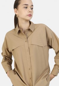 Lichtbeige button-up shirt met een gestructureerde kraag, twee borstzakken en lange mouwen. Bevat knoopdetails in een complementaire tint.