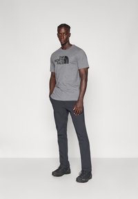 Camiseta gris con logo negro, pantalones oscuros y botas de senderismo negras. Corte ajustado, mangas cortas y diseño básico de cuello redondo.