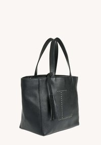 Sac en cuir noir avec deux poignées, un pompon décoratif et des clous dorés formant la lettre "L" à l'avant.